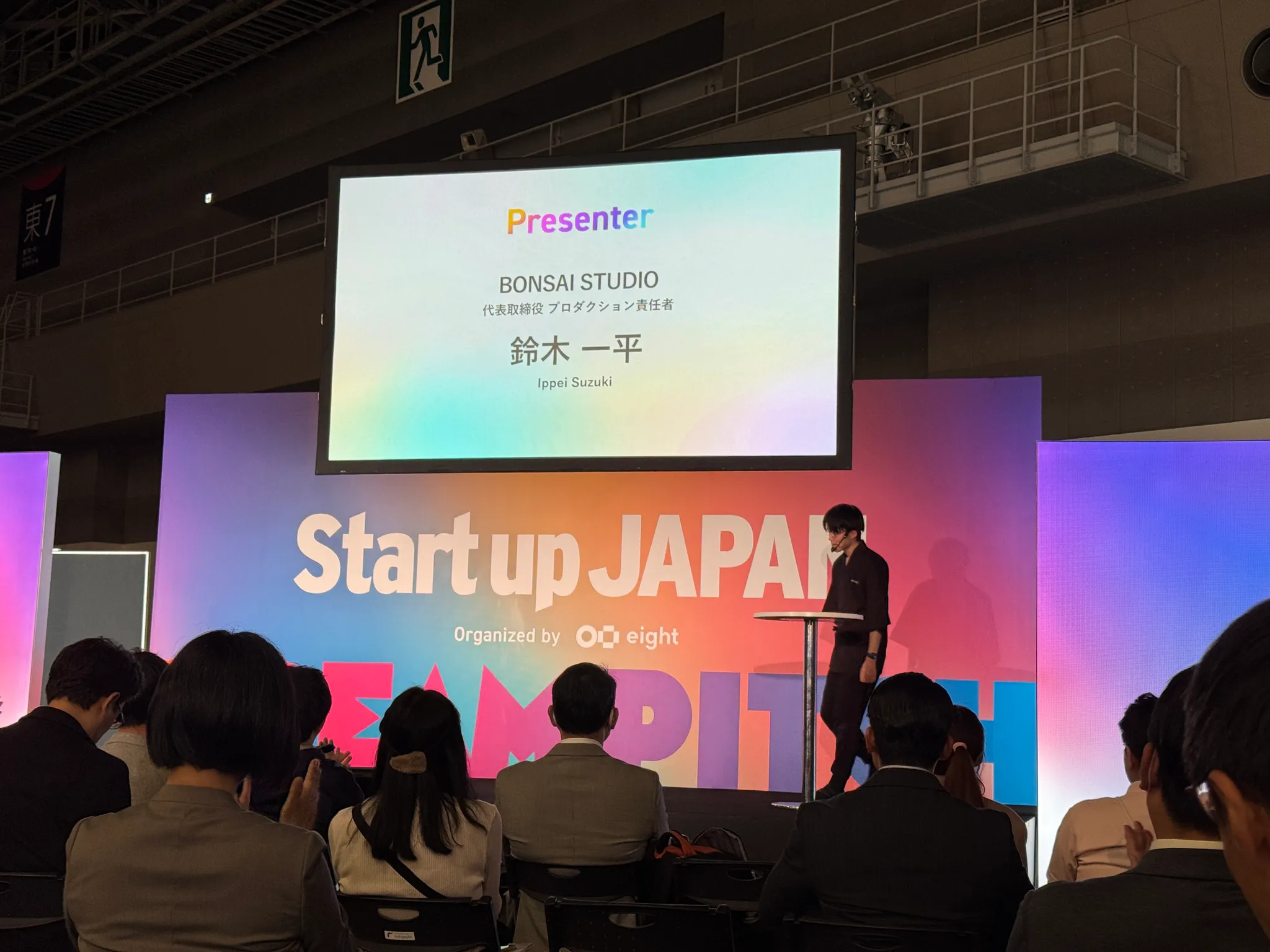 『Startup Japan』のステージ上でプレゼンテーションを行う男性の写真。スクリーンには「Presenter」や会社名「BONSAI STUDIO」などの文字が表示され、会場には多くの聴衆が座っている。