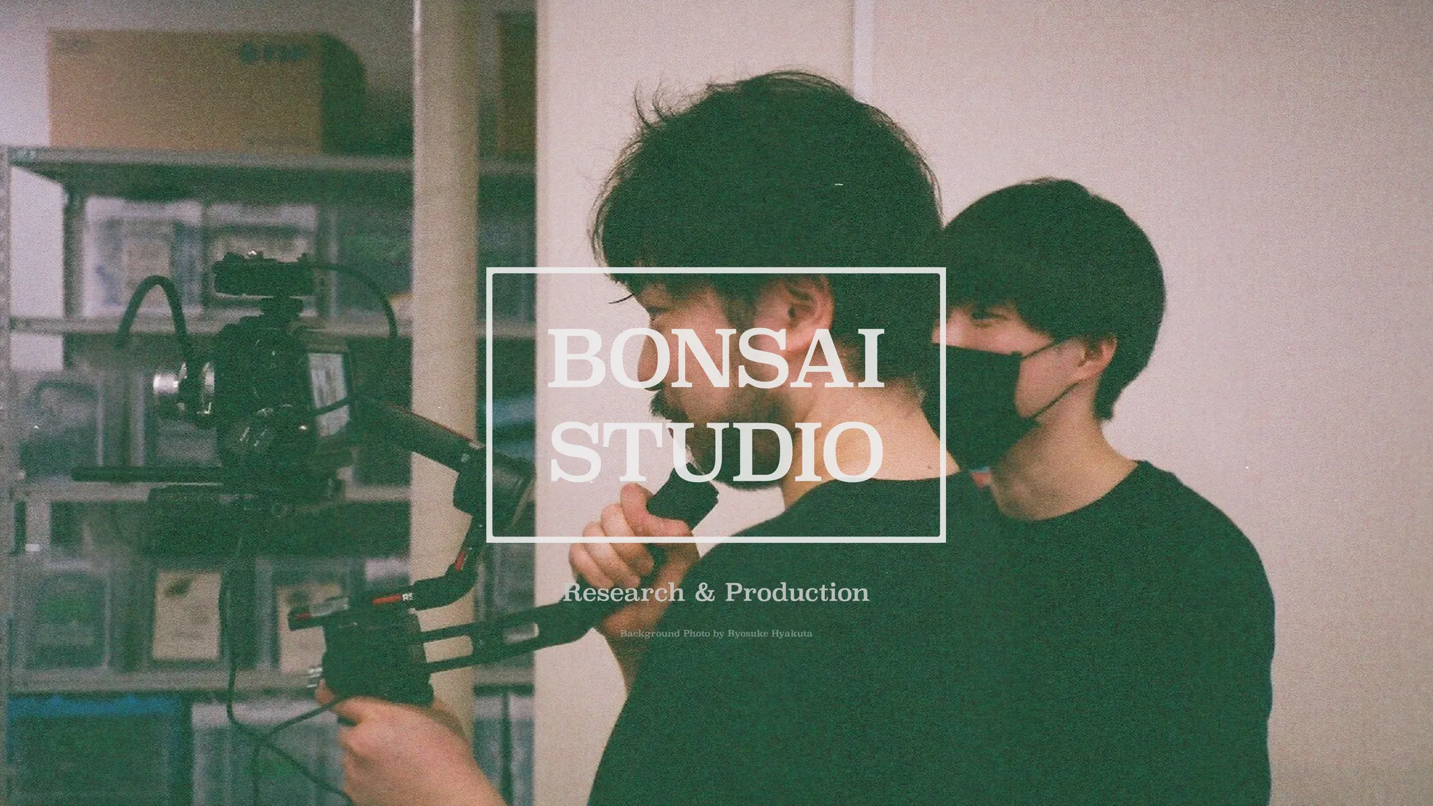 ジンバルにセットされたカメラを構える山本と鈴木の写真。手前に BONSAI STUDIO のロゴと，Research & Prodcution の文字。背景画像の撮影は Rysouke Hyakuta。