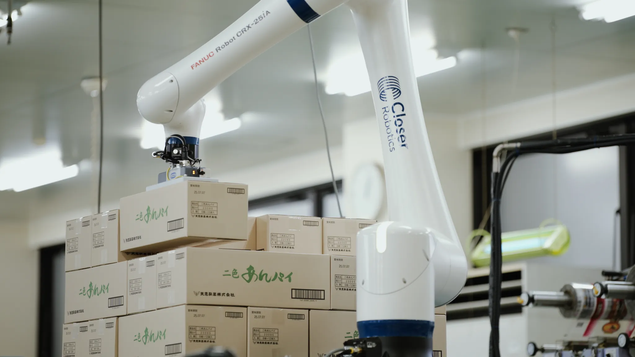 Closer RoboticsとFANUC Robot CRX-25iAと記された白いロボットアームが、段ボール箱を掴んで積み上げている様子。