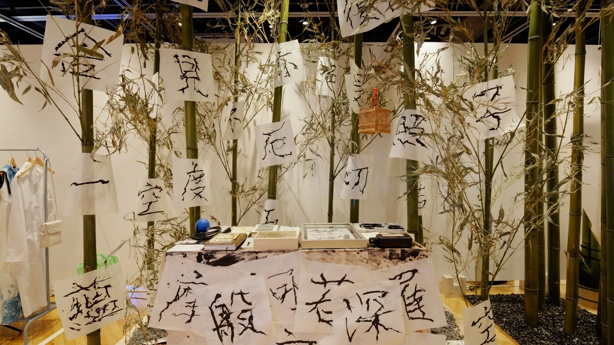 立てられた竹に多数の書道作品が吊るされ、手前の台の上にも書道道具や作品が並んでいる。