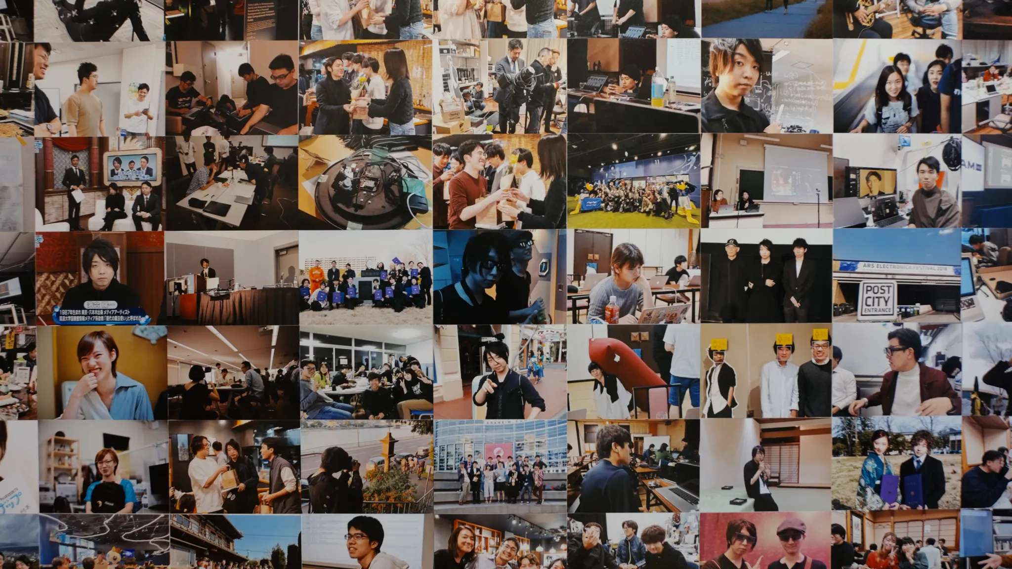 壁一面に貼られた多数の小さな写真のコラージュのクローズアップ。様々なイベントや人々、技術的な展示などが写っている。