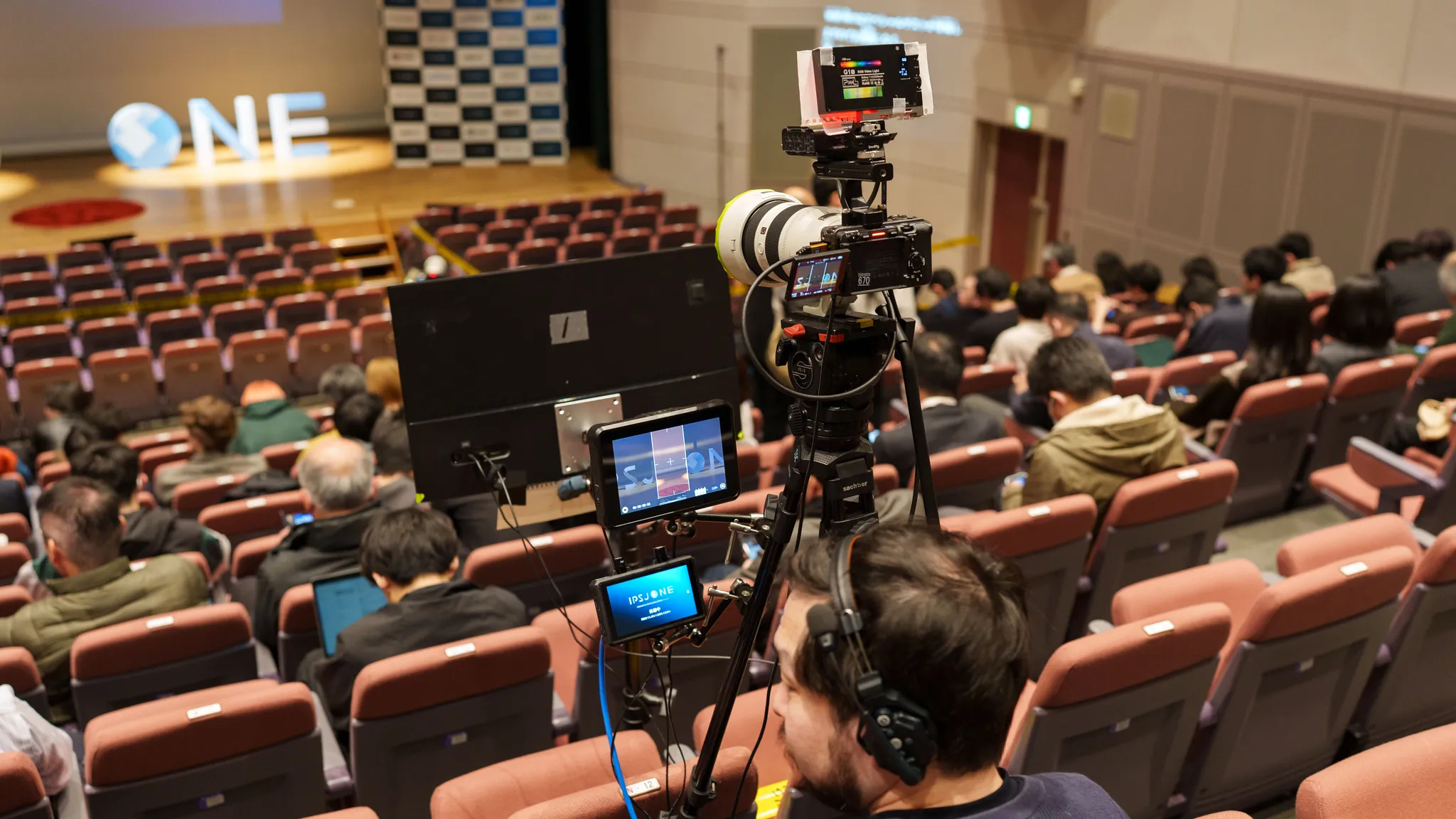 ホールの観客席で望遠レンズつきのカメラを操作するスタッフ。複数のモニタが設置されている。SONY ILME-FX3 と FE 50-150mm F2 GM の組み合わせ。