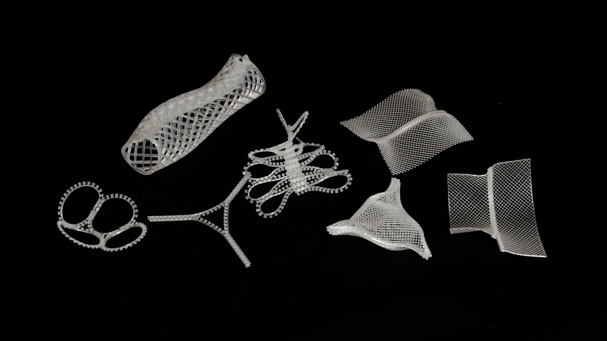 黒い背景に並べられた、筒状や平面など多様な形状の白い3Dプリントパーツ群。