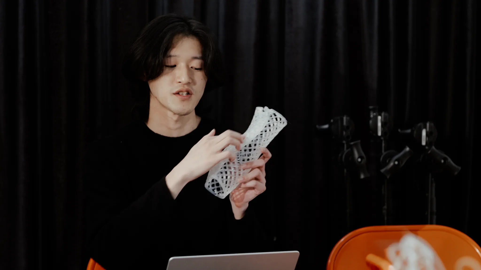 黒い服を着た人物（金田 昌也）が、手に持った白い網目状の物体を観察しながら話している。