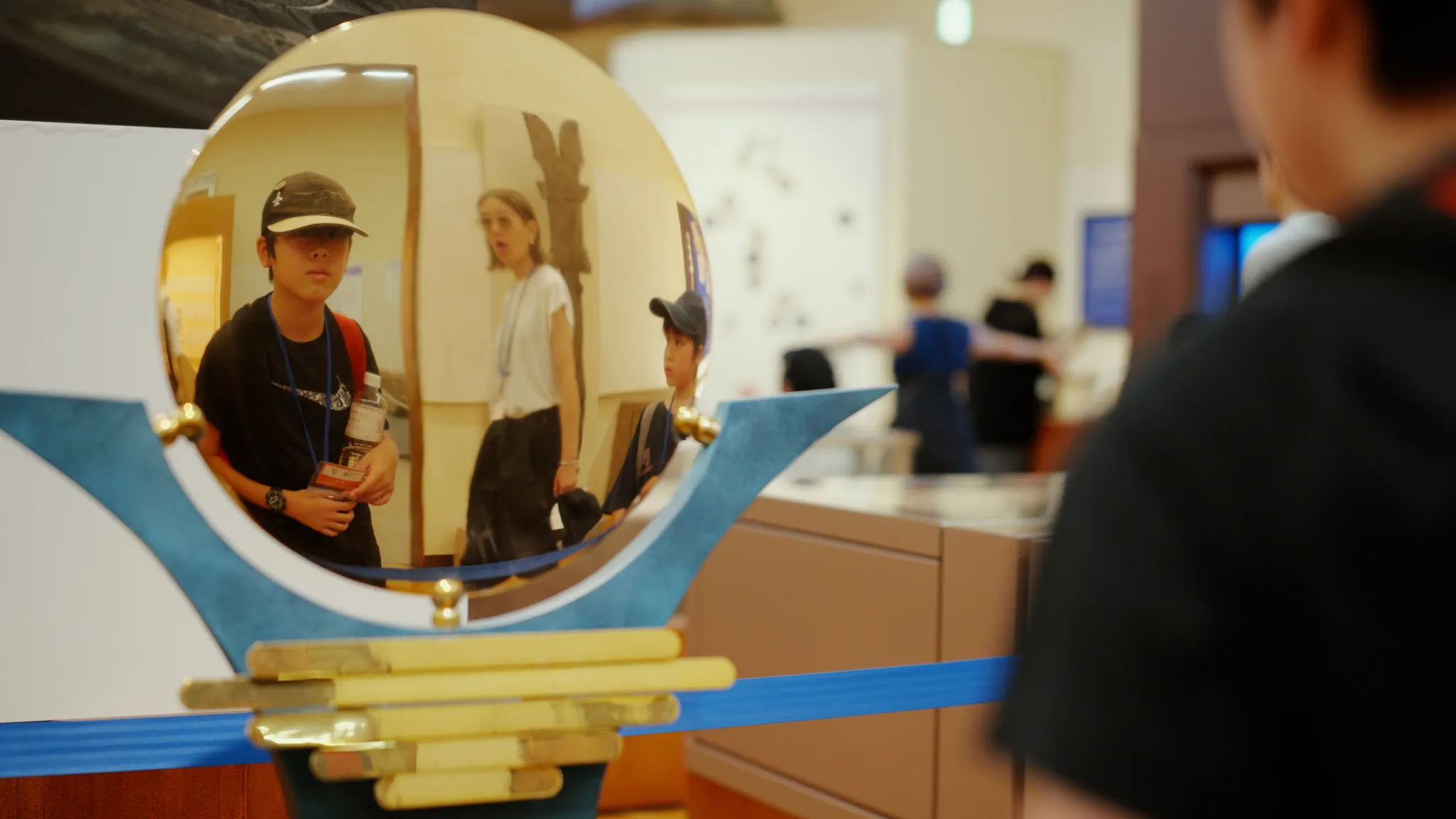 博物館の展示物である凸面鏡。鏡には見学している人々が映っている。