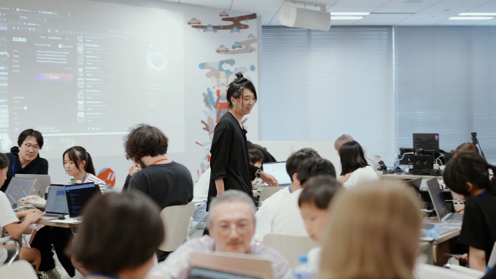 大勢の参加者がラップトップで作業するワークショップで、落合氏が様子を見ながら歩いている。