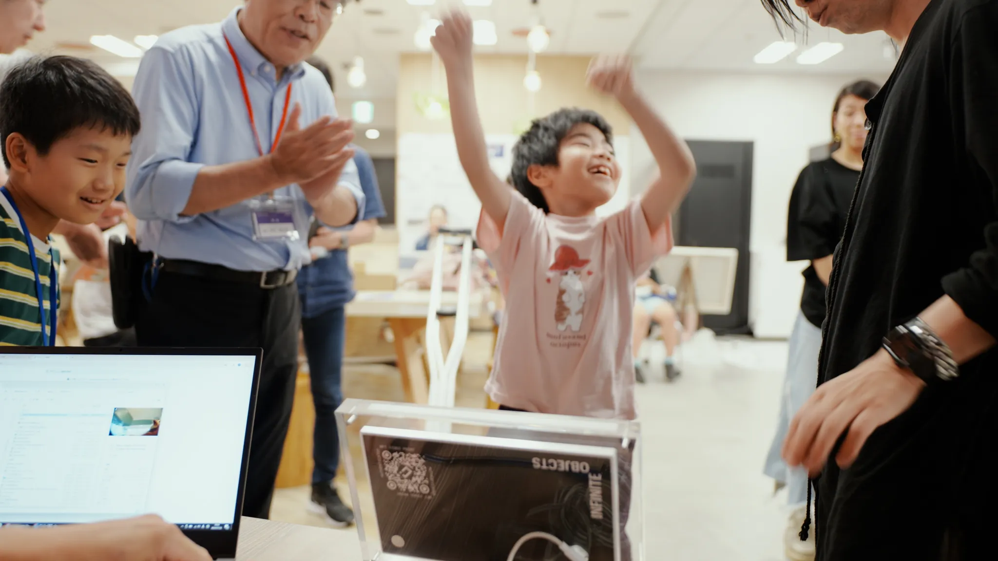 子どもが腕を上げて喜んでいる。周りの人々は拍手して笑顔を向けている。