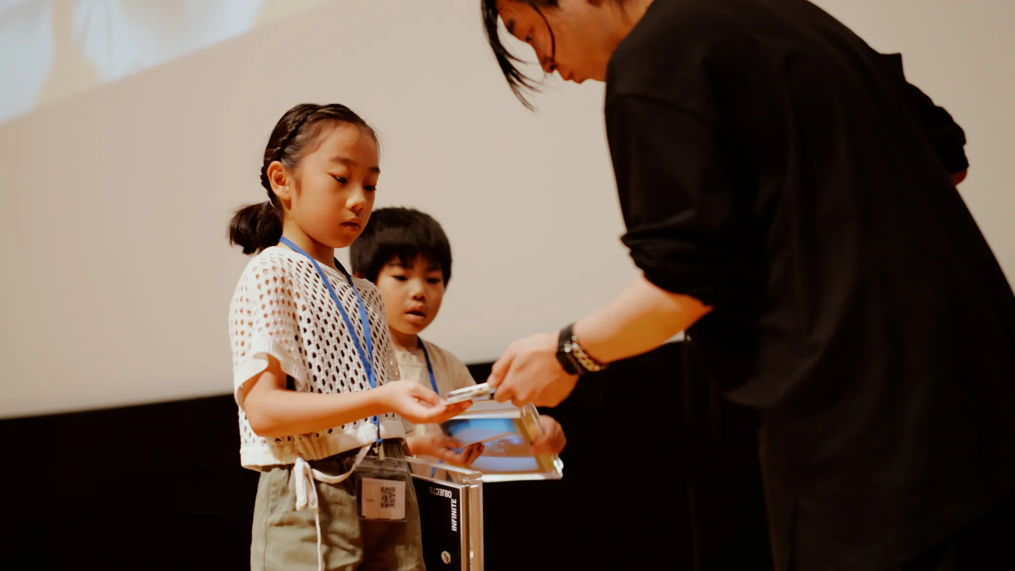 落合氏がスマートフォンを子どものハードウェアウォレットにかざし、卒業証明NFTを授与する様子。