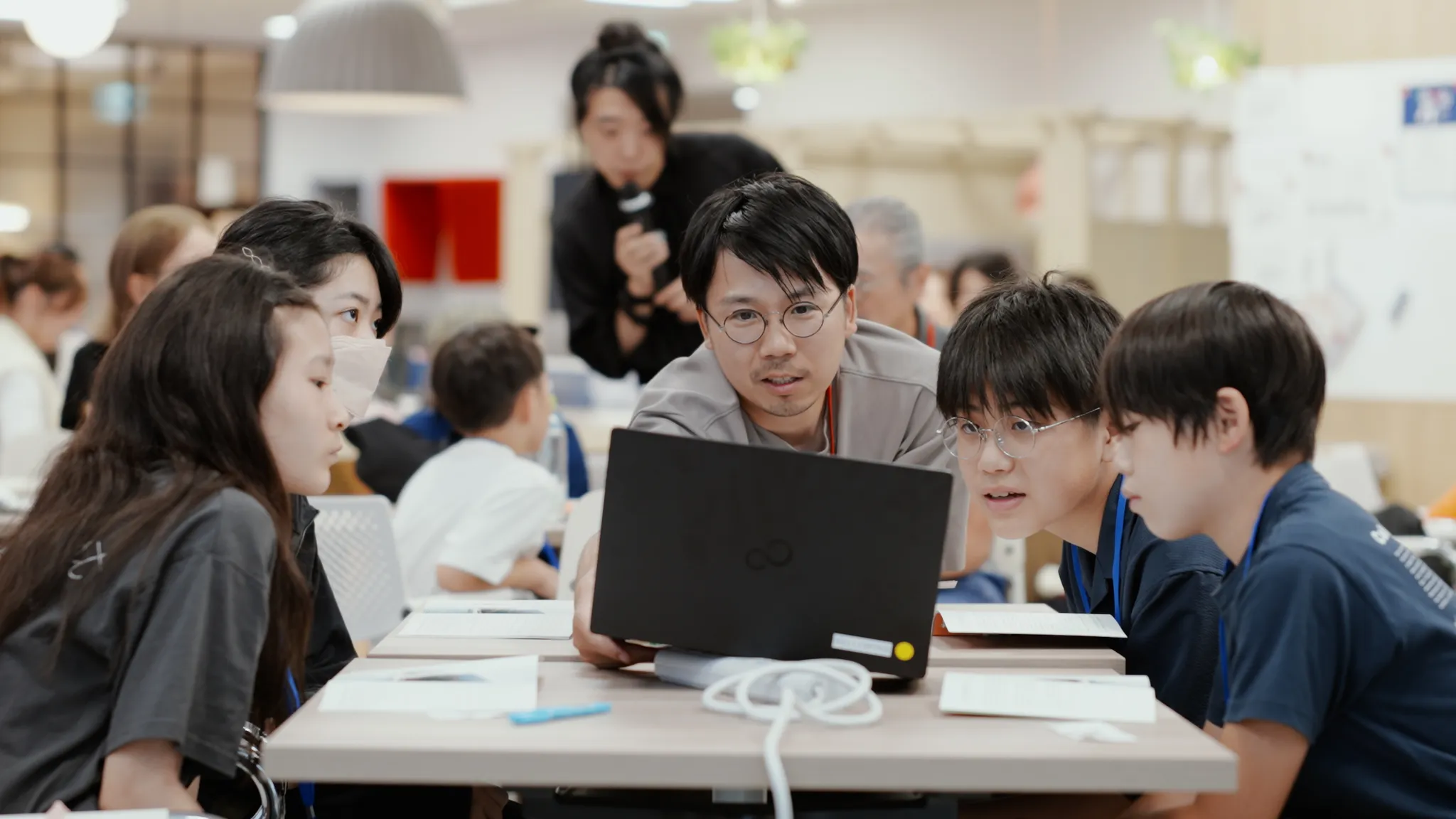 数人でノートパソコンを囲み、画面に表示されたものを覗き込む様子。