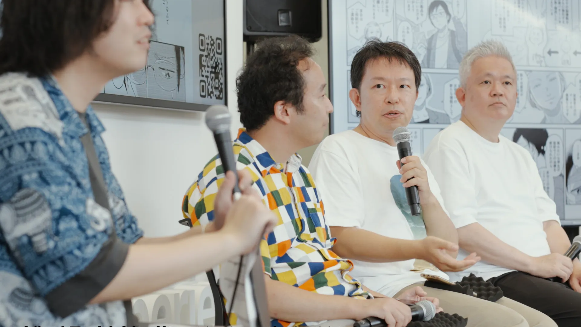 漫画のコマが映し出されたモニターを背景に、横一列に座ってパネルディスカッションを行う4人。左から、宮田龍、大澤博隆、倉田タカシ、金井良太。左から3番目の倉田氏がマイクを持って話している。