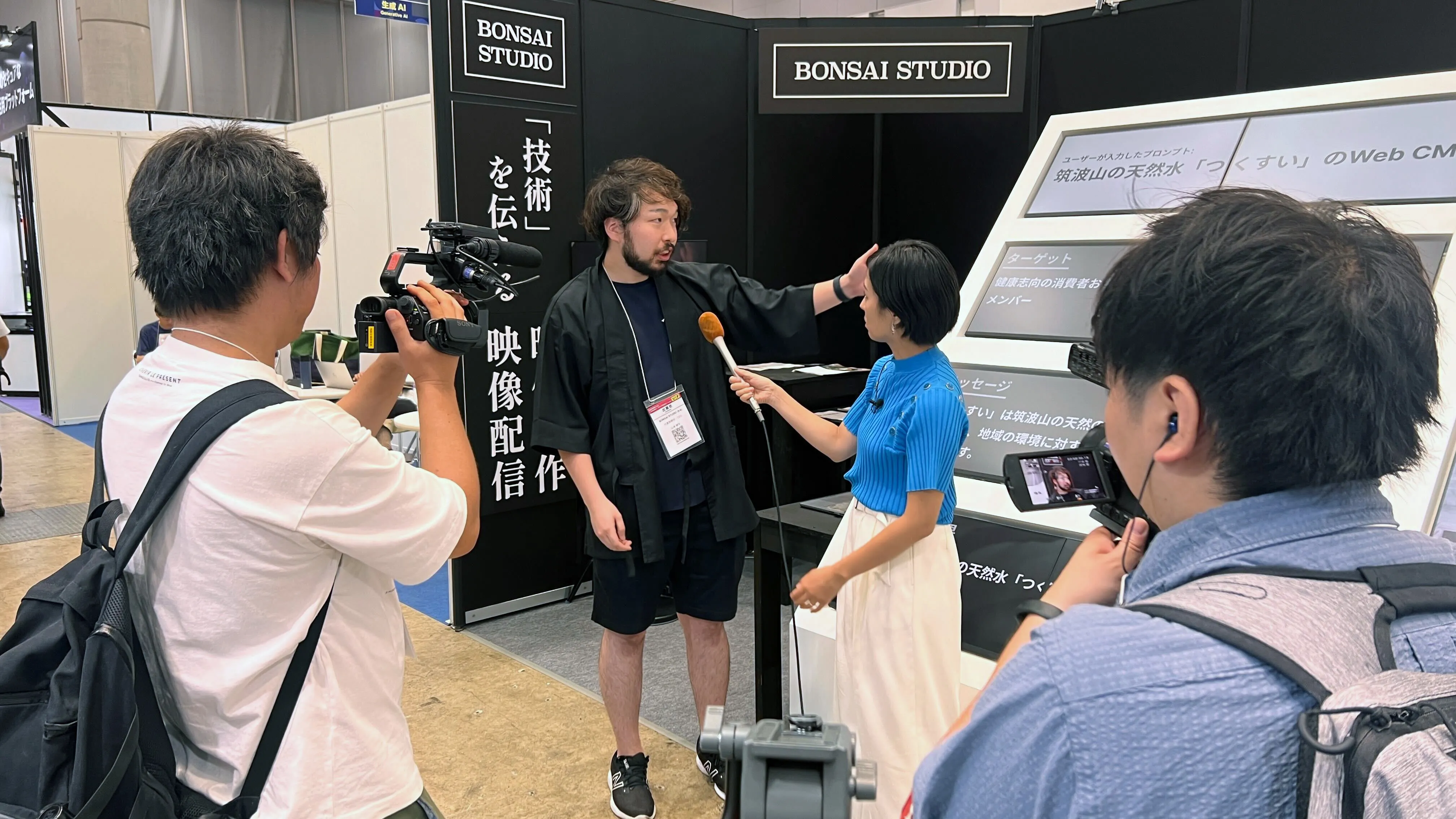 展示ブースの前で取材を受ける BONSAI STUDIO の山本健太
