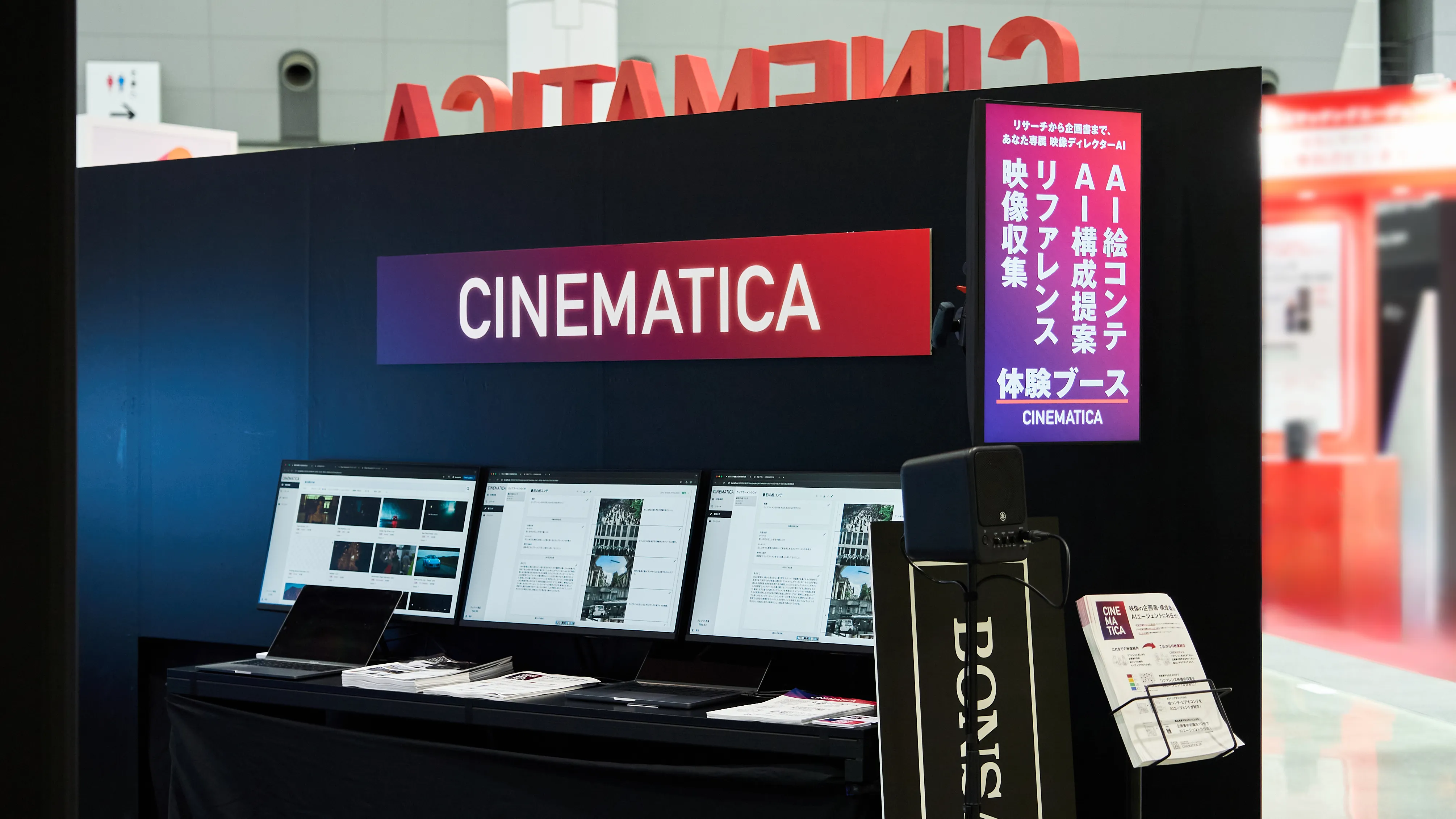 黒を基調とした「CINEMATICA」の展示ブース。3台のモニター、サービスを紹介する縦型デジタルサイネージ、パンフレットが設置され、映像制作AIツールの体験コーナーとなっている。
